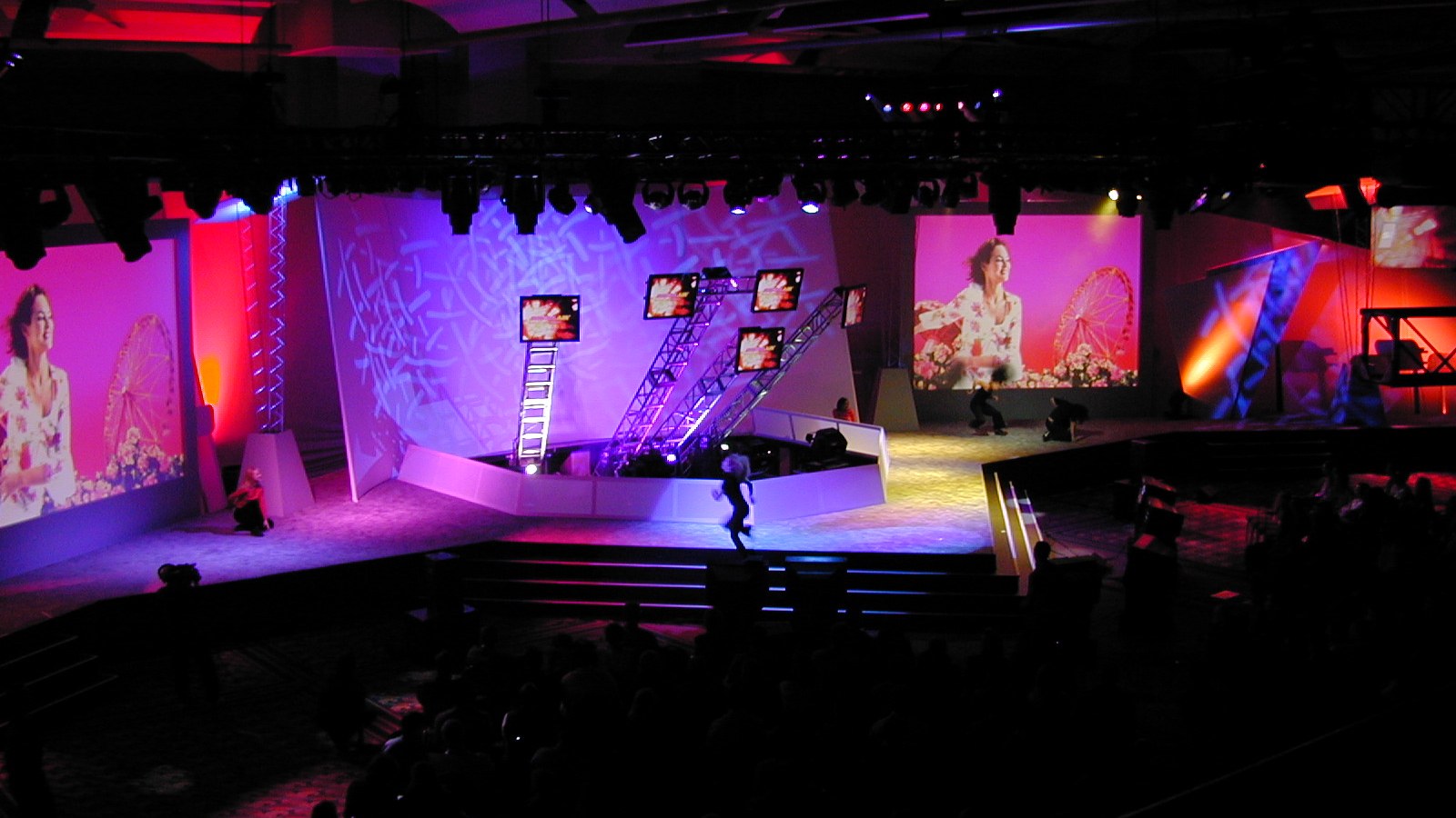 A purple-lit live production with sculptural scenery and large video screens.